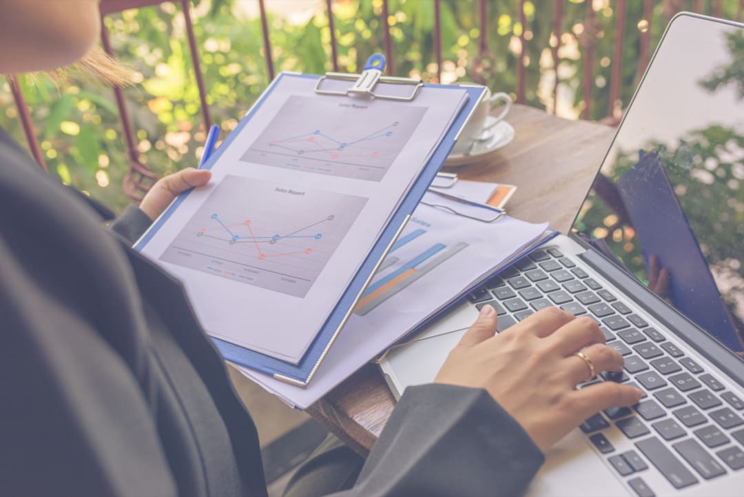 Small business owner ticking a website audit checklist next to a laptop showing a performance report