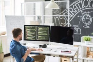 Web designer working at a desk with one screen showing a visual page layout and another showing code